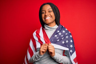 Bağımsızlık gününde Amerika Birleşik Devletleri bayrağı taşıyan genç, Afro-Amerikan vatansever bir kadın. Mutlu bir yüzle ayakta duruyor ve gülümsüyor.