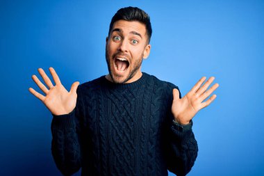 Genç ve yakışıklı bir adam mavi arka planda dikilip kollarını kaldırıp heyecanla haykırarak çılgın ve hayret verici başarılarını kutluyor. Kazanan konsept