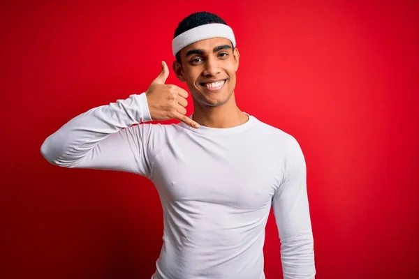 Young handsome african american sportsman wearing sportswear over red background smiling doing phone gesture with hand and fingers like talking on the telephone. Communicating concepts.