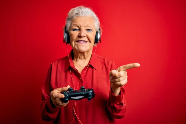 サイドに手と指で非常に幸せなポインティングジョイスティックとヘッドフォンを使用してビデオゲームをプレイシニア美しい白髪のゲーマーの女性 — ストック写真