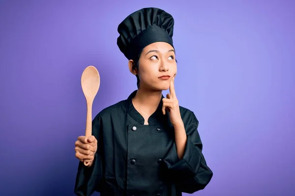 年轻美丽的中国厨师女士身穿炊具制服 头戴木勺 严肃地看待问题 非常迷惑的想法 — 图库照片