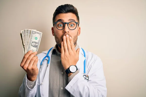 Młody Lekarz Trzyma Kupę Banknotów Dolara Odosobnionym Tle Usta Ręką — Zdjęcie stockowe