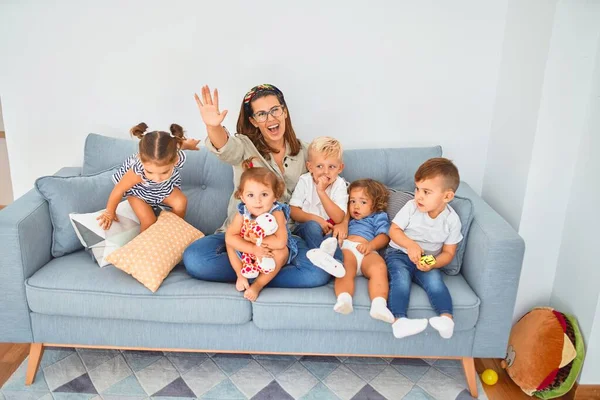 Beautiful teacher and group of toddlers sitting on the sofa playing at kindergarten