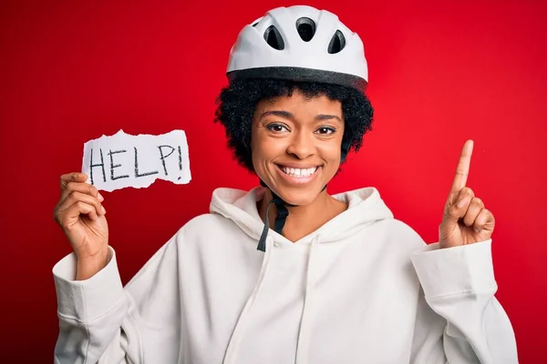 アフリカ系アメリカ人女性を着て巻き毛自転車ヘルメットを保持紙ヘルプメッセージで驚いてアイデアや質問を指差す指で幸せな顔 ナンバーワン — ストック写真