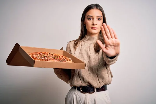 年轻美丽的黑发女子拿着盒子 用意大利披萨盖着白色的背景 张开手 严肃而自信地做着止步手势 做着防守动作 — 图库照片