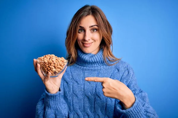 Jovem Bela Morena Segurando Tigela Com Amendoins Sobre Fundo Azul — Fotografia de Stock