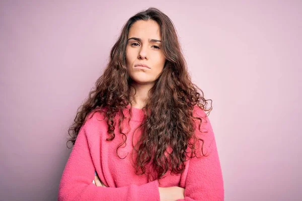 孤立したピンクの背景にカジュアルなセーターを着て巻き毛を持つ若い美しい女性は懐疑的で緊張し 両腕を組んで顔に不承認式 負の人 — ストック写真