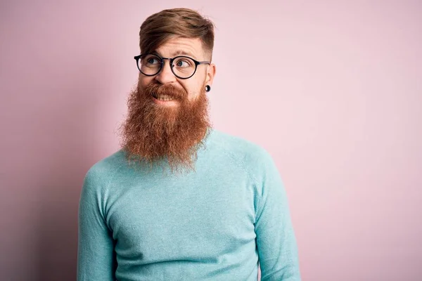 ハンサムなアイルランドの赤毛男あります髭を身に着けています眼鏡上のピンク隔離された背景笑顔側を見て離れて考え方 — ストック写真