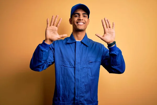 年轻的非洲技师 身穿蓝色制服 头戴黄色背景帽 头戴十号手指 面带微笑 自信而快乐 — 图库照片