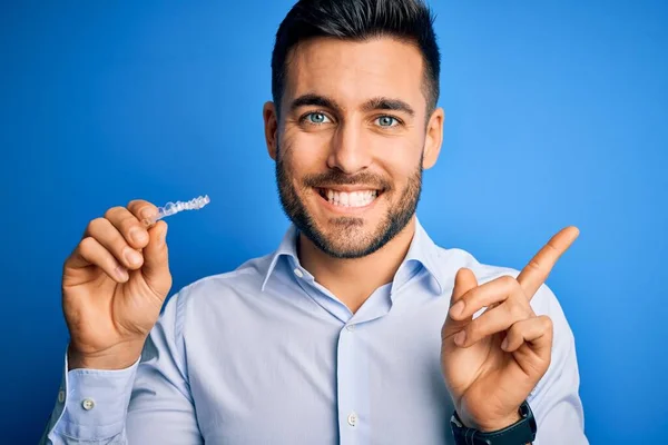 Junger Gutaussehender Mann Hält Zahnausrichterzahnkorrektur Über Blauem Hintergrund Und Zeigt — Stockfoto