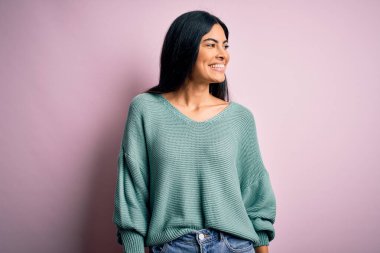 Pembe arka planda yeşil süveter giyen, yüzünde gülümseme ve doğal ifadeyle bir o yana bir bu yana bakan genç, güzel İspanyol moda kadını. Kendinden emin gülen.