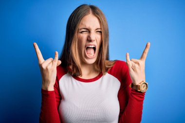 Genç, güzel, kızıl saçlı bir kadın izole edilmiş mavi arka plan üzerine gündelik tişört giyip çılgın bir ifadeyle elleri havada rock sembolü yaparak bağırıyor. Müzik yıldızı. Ağır konsept.