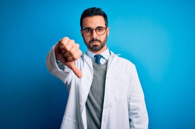 Mavi arka planda sakallı ve gözlüklü yakışıklı doktor mutsuz ve sinirli görünüyor. Reddedilmiş ve olumsuz bir hareket yapıyor. Kötü ifade.