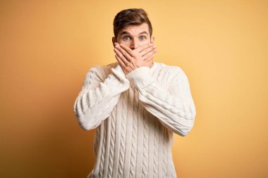 Sarışın, sakallı, mavi gözlü, sarı arka planda beyaz kazak giyen genç bir adam ağzını yanlışlıkla ellerle kapatmış. Gizli konsept.