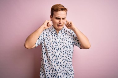 Genç, yakışıklı, yaz gömleği giyen, pembe arka planda duran, yüksek sesli müzik sesi için rahatsız edici ifadeleri olan kulakları parmaklarıyla kaplayan genç bir adam. Sağır kavramı.