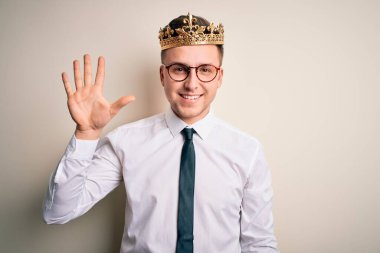İzole edilmiş arka planda altın taç takan yakışıklı beyaz iş adamı beş numarayı işaret ederken kendinden emin ve mutlu bir şekilde gülümsüyor..