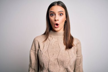 Genç, güzel, esmer bir kadın beyaz arka plan üzerinde dikilmiş korku, korku ve heyecan dolu bir yüz ifadesiyle şok olmuş ve korkmuştu..