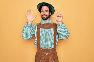 Almanya Festivali için geleneksel Alman Ekim Festivali kıyafeti giyen yakışıklı genç adam yedinci parmaklarını gösterip gösterirken kendinden emin ve mutlu gülümsüyor..