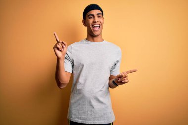 Yakışıklı Afro-Amerikan sporcu sarı arka planda spor giysisi giyiyor ve parmaklarıyla farklı yönleri işaret ederek gülümsüyor. Reklam için boşluk kopyala