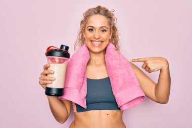 Güzel, sarışın, spor yapan, havlu tutan, protein içeceği sallayan, mutlu ve gururlu bir kadını işaret eden bir kadın.