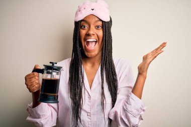 Genç Afrikalı Amerikalı kadın pijama giyip geceleri kahveyi yoruyor çok mutlu ve heyecanlı, kazanan ifade zaferi büyük bir gülümsemeyle kutluyor ve ellerini kaldırıyor