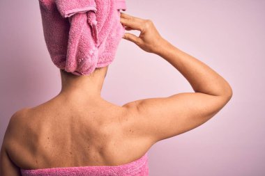 Orta yaşlı esmer kadın, pembe arka planda siyah bir maske takıyor. Geriye doğru, elleri kafasında şüpheyi düşünüyor.