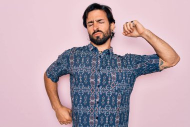 Genç, yakışıklı, bohem, pembe arka planda hippi tarzı giyinmiş yorgun ve rahat, uykulu ve sabahın erken saatleri için esniyor.