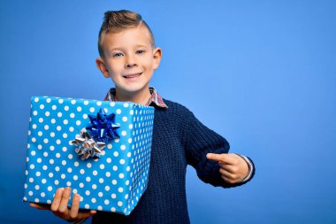 Küçük beyaz çocuk doğum günü ya da Noel hediyesi olarak sürpriz bir kutu tutuyor. El ve parmağıyla işaret ederek çok mutlu.