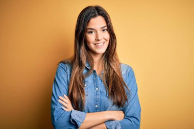 İzole edilmiş sarı arka plan üzerinde dikilmiş kollarını kavuşturup kameraya bakan genç ve güzel bir kız. Pozitif kişi.