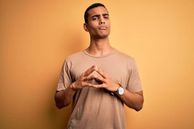 Sarı arka plan üzerinde sıradan tişörtler giyen genç ve yakışıklı Afro-Amerikan erkeği ellerini birleştirip gülümseyerek gevşemiş ve neşeli olmasını diliyordu. Başarı ve iyimser