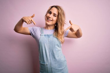 Genç, güzel, sarışın bir kadın pembe arka planda dikilmiş, kendine güvenen, gururlu ve mutlu parmakları olan bir kadın..