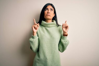 İzole edilmiş arka planda yeşil süveter giyen genç ve güzel İspanyol kadın üzgün ve üzgün görünüyor, parmaklarıyla yön gösteriyor, mutsuz ve depresif..