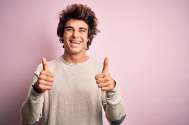 İzole edilmiş pembe arka plan başarısı tabelasının üzerinde duran ve el hareketleriyle olumlu jest yapan, gülümseyen ve mutlu genç, yakışıklı bir adam. Neşeli ifade ve kazanan jest.