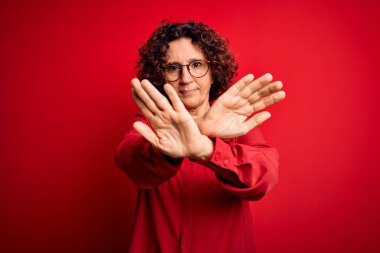 Orta yaşlı, kıvırcık saçlı, rahat gömlekli, kırmızı arka planda gözlüklü güzel bir kadın.