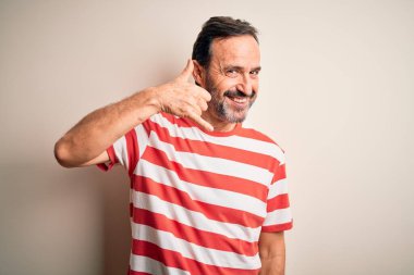 Sıradan çizgili tişört giyen orta yaşlı beyaz bir adam izole edilmiş beyaz arka planda durup el ve parmaklarıyla telefon hareketleriyle telefonda konuşur gibi gülümsüyor. İletişim kavramları.