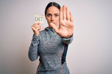 Spor kıyafetleri giyen, spor kıyafeti giyen, elinde diyet sözcüğüyle dur işareti yapan, ciddi ve kendinden emin bir ifade sergileyen, savunma jesti olan genç bir fitness kadını.