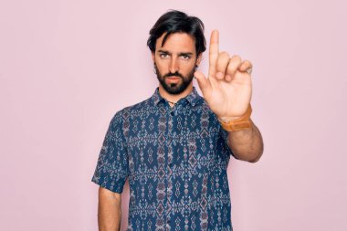 Pembe arka planda hippi tarzı giyinmiş genç, Latin asıllı bohem bir adam. Parmağını kaldırmış ve kızgın bir ifade sergiliyor.
