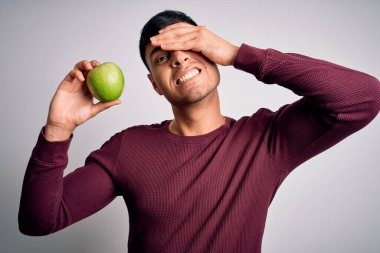 Genç İspanyol adam taze yeşil elma yiyor. Tecrit edilmiş arka planda sağlıklı beslenme olarak. Kafa kafaya verilmiş, utanç ve şaşkınlık dolu, sinirli ve hayal kırıklığına uğramış bir şekilde. Hata için korku ve üzüntü.