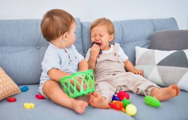 Güzel bebekler, biri ağlıyor, kanepede oturuyor, evde oyuncaklarla oynuyor.