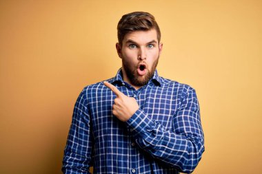 Sarışın, sakallı, mavi gözlü, sarı arka planda gömlek giyen genç bir işadamı..