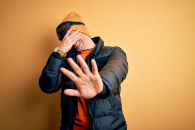 Genç yakışıklı kayakçı kar maskesi takarak kayak yapıyor. Kar gözlüğü takıyor, gözlerini elleriyle kapatıyor ve üzgün ve korku ifadeleriyle jest yapıyor. Utanç verici ve olumsuz bir kavram..