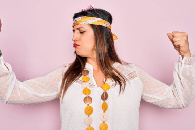Genç İspanyol hippi kadın pembe arka planda moda şapkası takıyor ve güneş gözlüğü takıyor. Kollarında gururla gülümseyen kaslar var. Fitness konsepti.