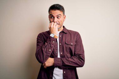 İzole edilmiş beyaz arka plan üzerinde sıradan bir tişört giyen genç yakışıklı elleri ağız yiyen tırnak üzerinde gergin ve stresli görünüyor. Endişe sorunu.