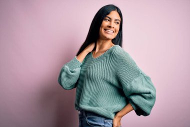 Moda kıyafetleri giyen genç ve güzel bir kadın. Manken, sokak tarzı giyiniyor. Pembe arka planda dikiliyor.
