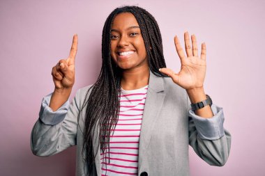 Genç Afrikalı Amerikalı iş kadını pembe izole edilmiş arka planda duruyor ve altı numaralı parmaklarıyla işaret ederken kendinden emin ve mutlu gülümsüyor..