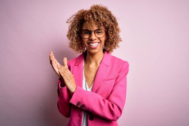Genç Afrikalı Amerikalı iş kadını pembe arka planda duran gözlük takıyor ve alkışlıyor ve mutlu, mutlu, gururlu elleri alkışlıyor.