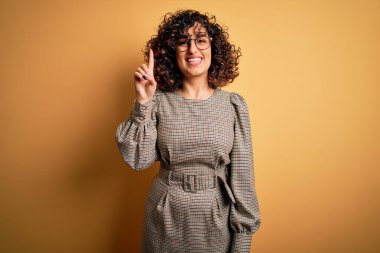 Güzel bir Arap iş kadını. Elbise ve gözlük takıyor. Sarı arka planda duruyor..