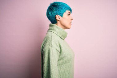 Mavi saçlı, normal balıkçı yaka kazak giyen rahat bir profil pozu veren, kendine güvenen bir gülümsemesi olan genç ve güzel bir kadın..