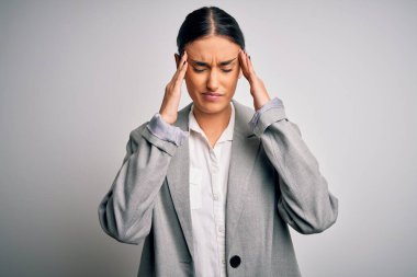 Beyaz arka plan üzerinde duran ceketli genç ve güzel esmer iş kadını. Ağrı ve migren yüzünden baş ağrısı çekiyor. Ellerini başının üstüne koy..
