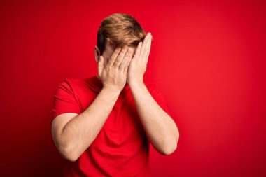 İzole edilmiş kırmızı arka plan üzerine gündelik tişört giyen genç ve yakışıklı bir adam. Ağlarken suratını ellerle kapatan üzgün bir ifade. Depresyon kavramı.